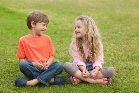 Two smiling kids sitting on the grass at the park