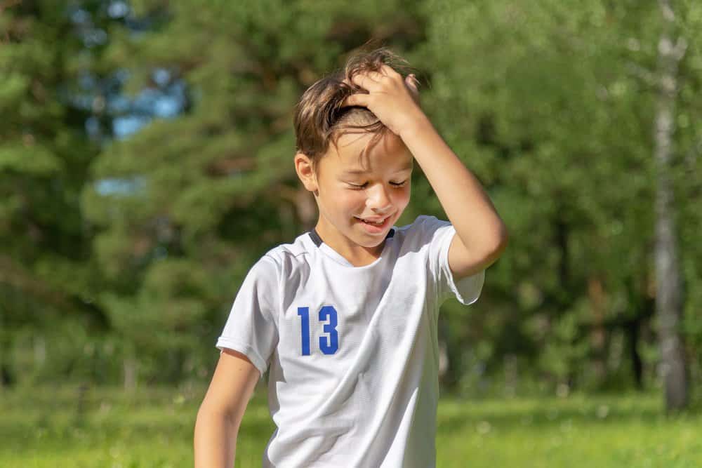 Smiling young boy in white athletic t-shirt with number 13 and touching his hair on nature background
