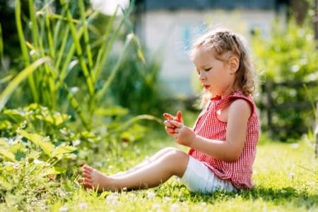 Cute baby girl sitting on the lawn in the garden while looking at strawberries in her hand