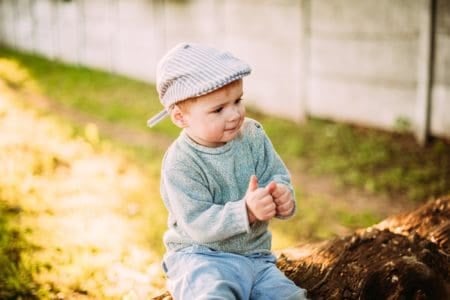 Cute toddler boy wearing beret sitting on tree trunk on sunny day