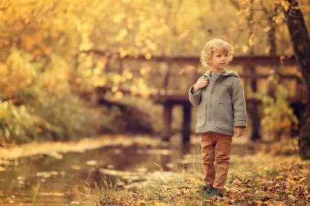 Little boy standing near pond in the autumn park