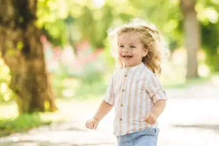 Cute little boy with curly blonde hair playing in park