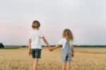 Brother and sister in a mowed field of wheat while holding hands
