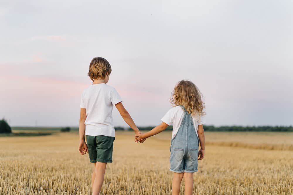 Brother and sister in a mowed field of wheat while holding hands