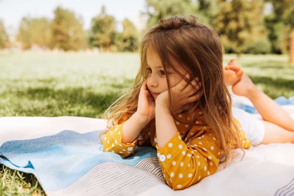 Cute little girl lying and relaxing on the blanket at the green grass