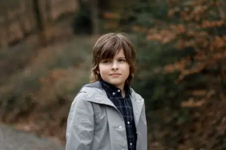 Handsome young boy with long hair in autumn forest