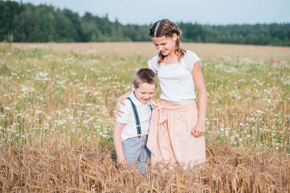 Two adorable siblings in the middle of spring field with daisy flowers