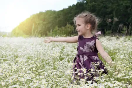 Cheerful girl in beautiful dress in the middle of daisy field
