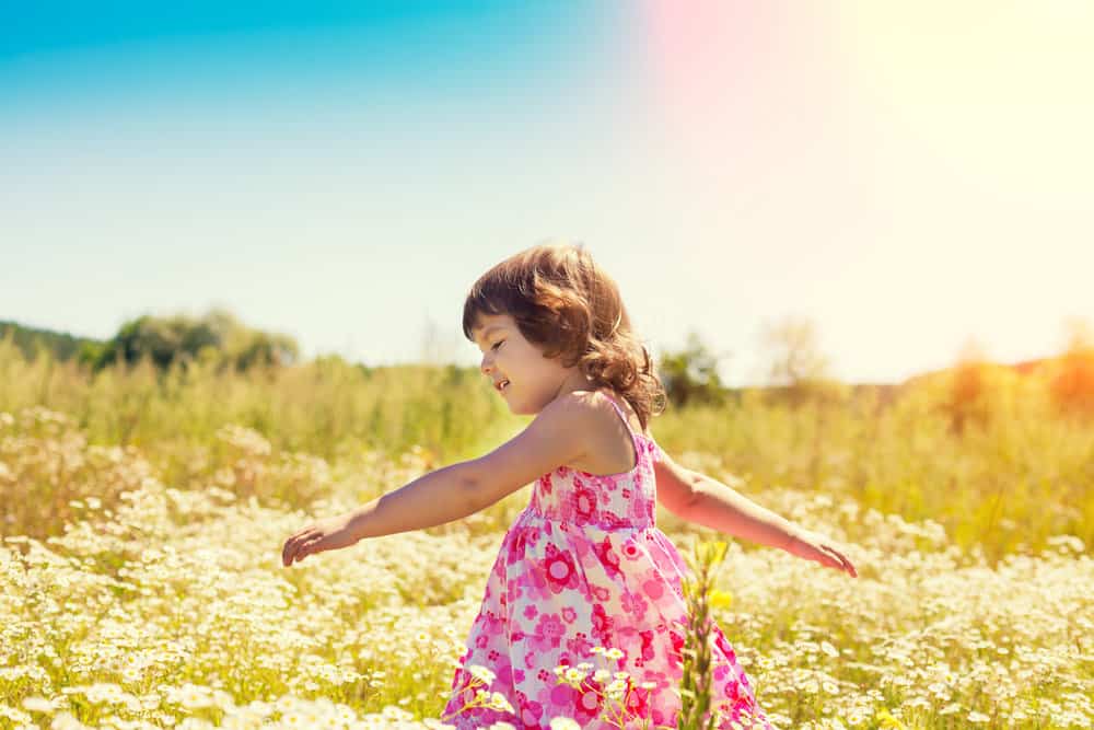 Cheerful little curly-haired girl walking on flower field