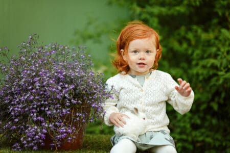 Little beautiful red-haired girl baby girl smiling and holding a rabbit in hands
