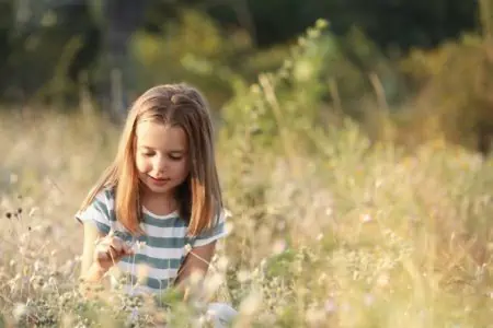 Adorable young girl playing with flowers in green meadow on sunny day