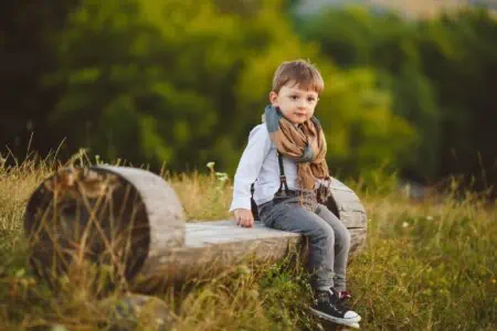Cute young boy sitting on wooden chair in autumn field