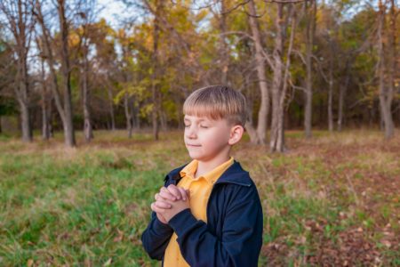 Little boy doing pray gesture outdoors