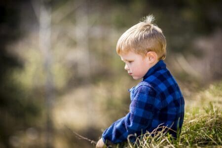 Blonde little boy in plaid jacket sitting on the grass