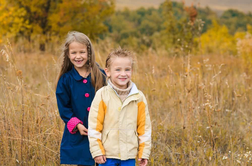 Adorable brother with sister on walk through autumn meadow