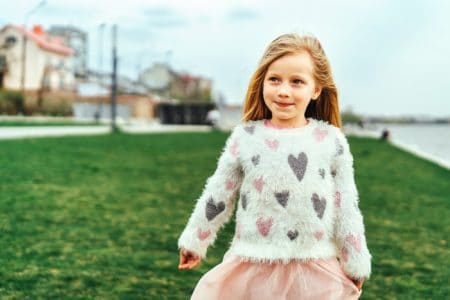 Adorable little girl in sweater standing outdoors in the park