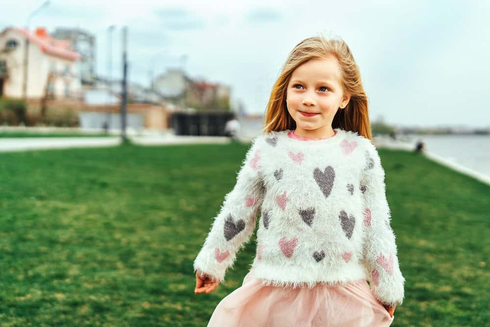 Adorable little girl in sweater standing outdoors in the park