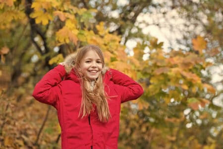 Cheerful girl wearing jacket with hood in autumn park