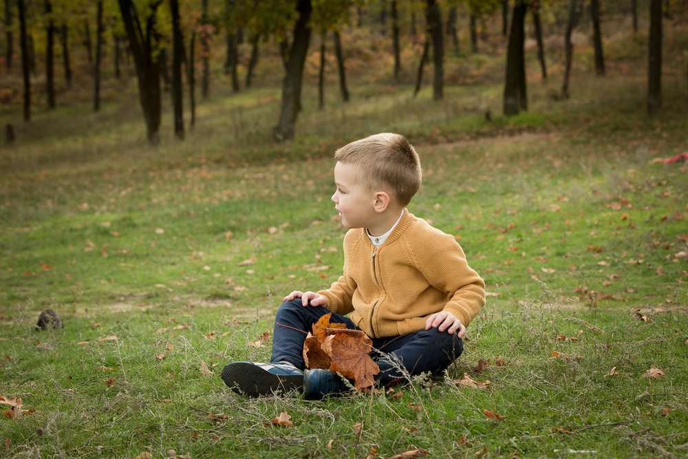 Little boy sitting on the ground in the autumn forest