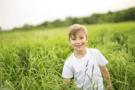 Cheerful boy in white tshirt standing in green meadow