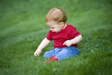 Little toddler boy redheaded baby boy sitting outside on grass