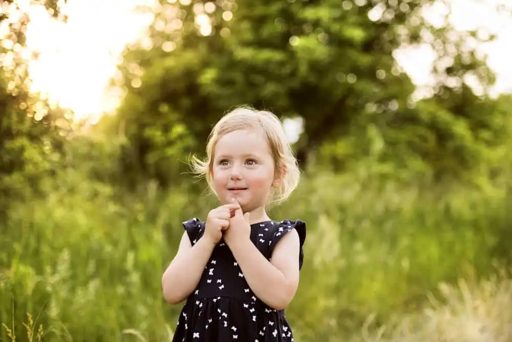 Cute little blonde girl in blue dress outside in the meadow