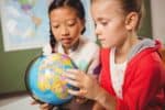 Two young girls studying the globe at school