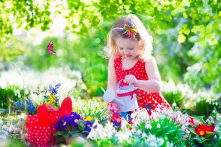 Little girl in a red dress watering flowers in the garden