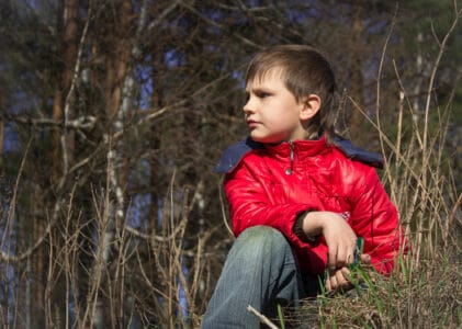Young boy wearing red jacket sitting on the grass looking sideways