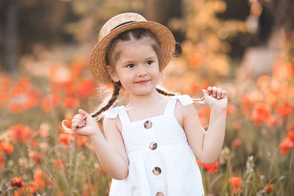 Smiling adorable girl wearing straw hat and white dress in flower field
