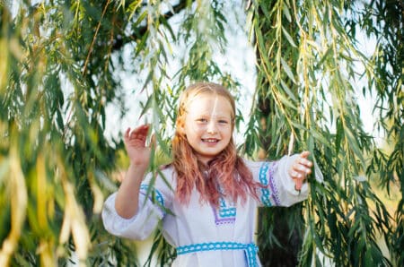 Cheerful little girl smiling to the camera under tree on sunny day