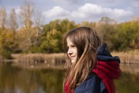 Pretty girl with long hair wearing jacket near the lake shore during autumn