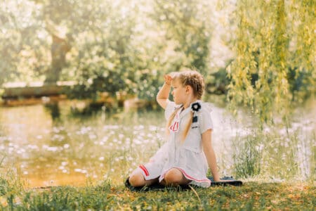 Cute girl with pigtails sits on the grass in the summer near the river