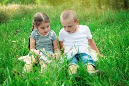 Two adorable kids reading book while sitting on the grass ground