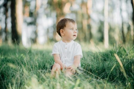 Cute little toddler boy sitting on the grass in the forest park