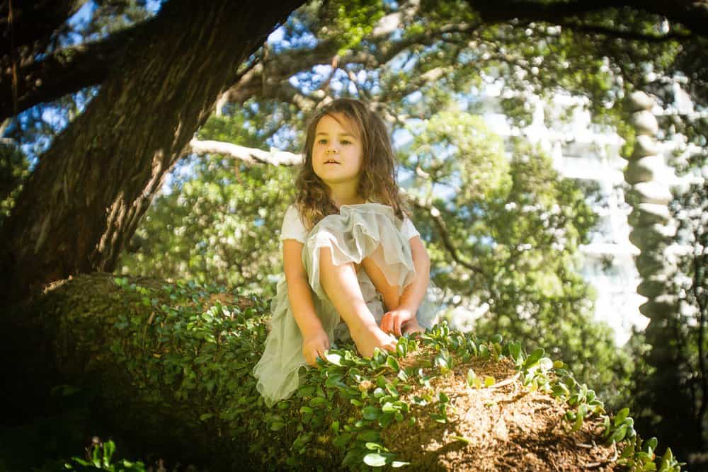 Beautiful little young girl sitting on tree branch in the forest