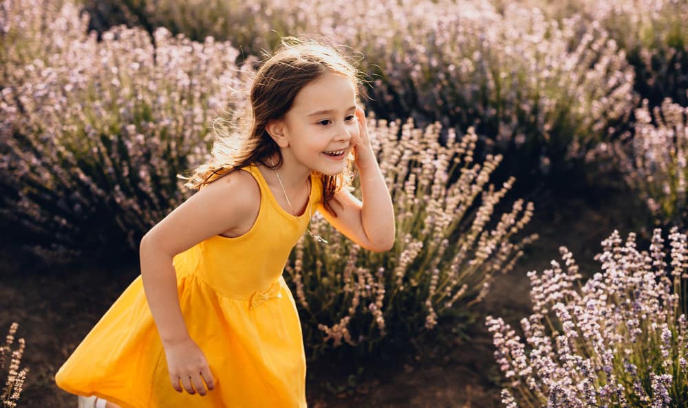 Lovely young girl wearing yellow dress playing in lavender field
