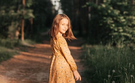 Beautiful young girl wearing floral dress posing standing in the forest during sunset