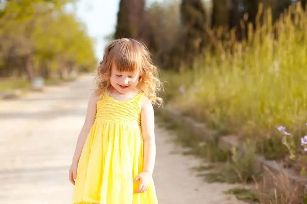 Little girl in yellow dress standing in the middle of the road
