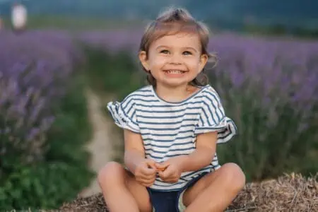 Adorable smiling little girl sitting on hay by the lavender field
