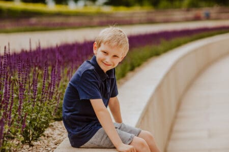 Young cute blond haired boy in blue summer shirt posing in the park with lavender