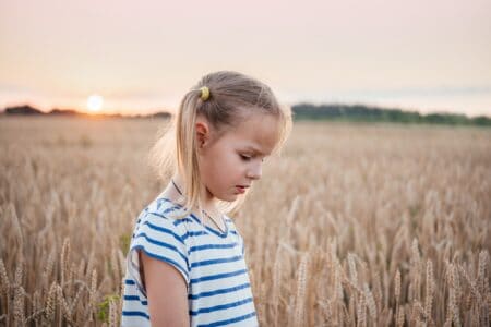 Little girl in the yellow wheat field at sunset summer landscape