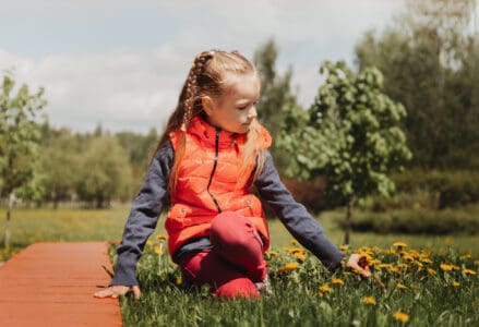 Cute little girl wearing puff jacket picking dandelion flowers in the park