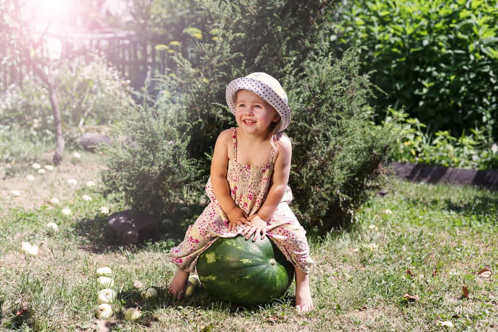 Cheerful girl wearing cap sitting on big watermelon