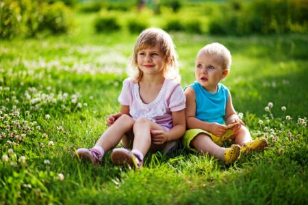 Little girl and boy sitting on the grass in the park