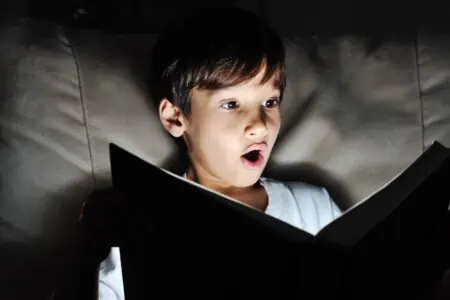 Little boy reading a book in the dark room