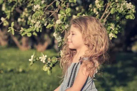 Little blond girl standing under a cherry tree