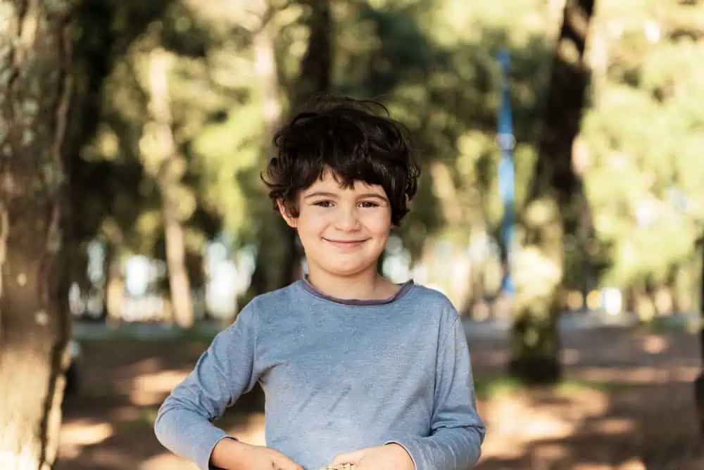 Smiling young kid with curly black hair in the forest