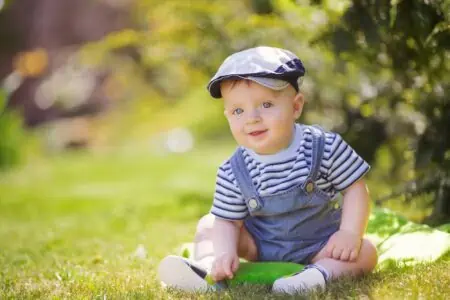 Adorable little boy wearing hat sitting on the grass in the park