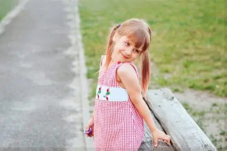 Little smiling girl with two ponytails in red dress posing outside